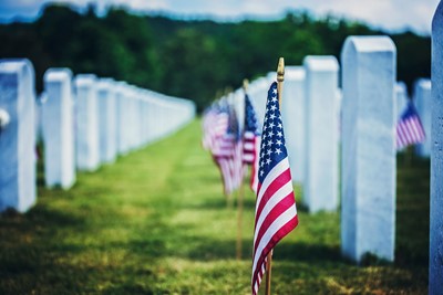 Memorial Day 2024, Rows of white military grave markers with American flags placed at the base, honoring fallen soldiers at a national cemetery on Memorial Day